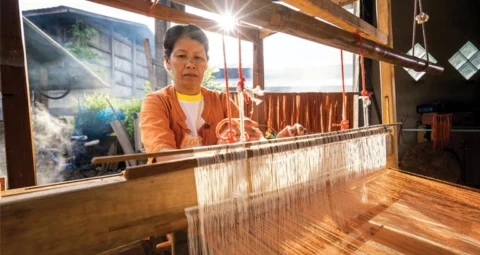 An artisan weaving textiles on a traditional wooden loom.