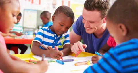 A teacher and young students coloring together in a classroom.