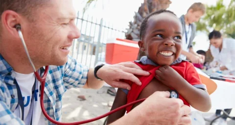A healthcare volunteer examining a smiling child with a stethoscope.