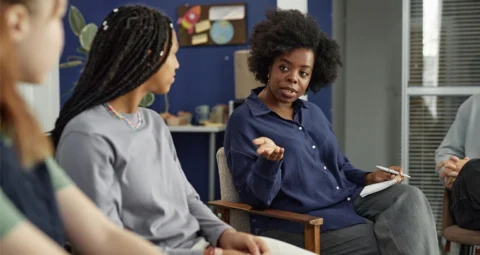 A facilitator leading a small group discussion in a community room.