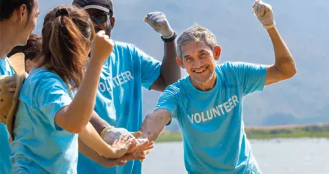 A diverse group of smiling volunteers stacking their hands together in celebration.