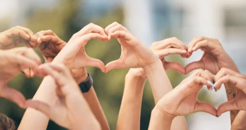 A diverse group of people making heart shapes with their raised hands.