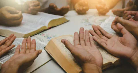 A group of people praying together around open religious books.
