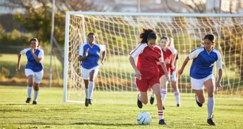Young women playing a competitive game of soccer on an outdoor field.